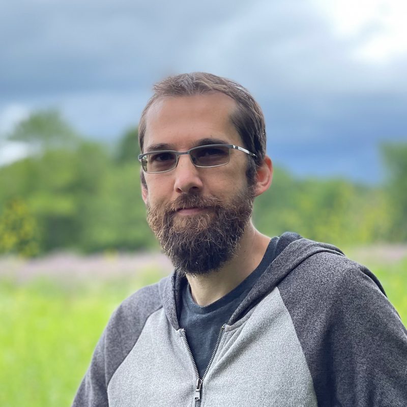 Jeff Schiller, founder of Rellihcs Services, standing outdoors in a green meadow under a cloudy sky